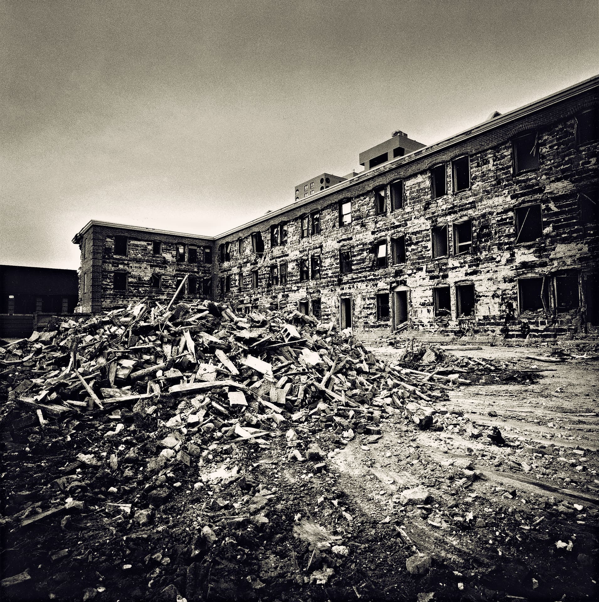 Long brick apartment block gutted to empty window openings behind a heaped mound of splintered timber and masonry rubble