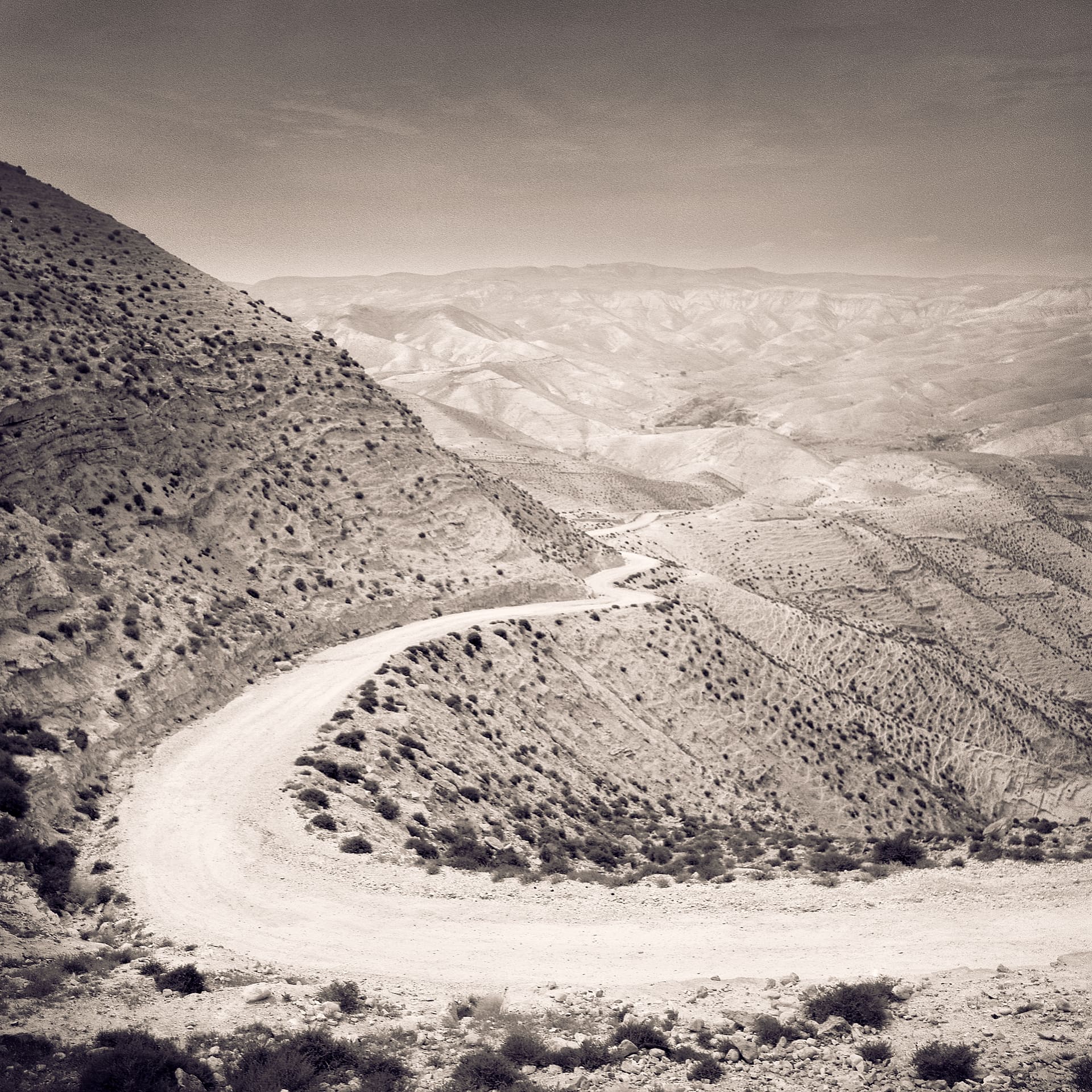 Unpaved road curving in a tight hairpin around a scrub-dotted desert hillside above receding arid ridges