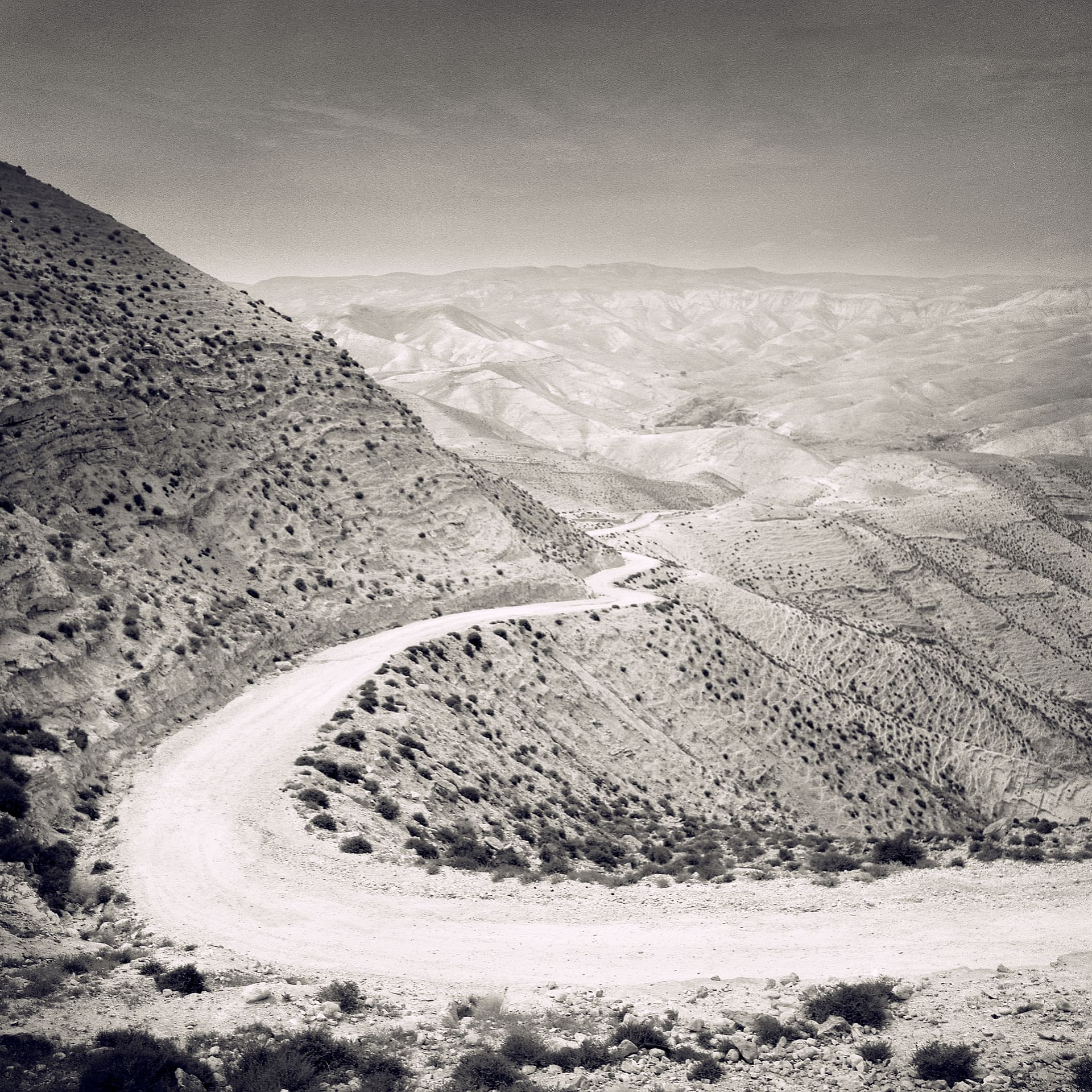 Unpaved road curving in a tight hairpin around a scrub-dotted desert hillside above receding arid ridges