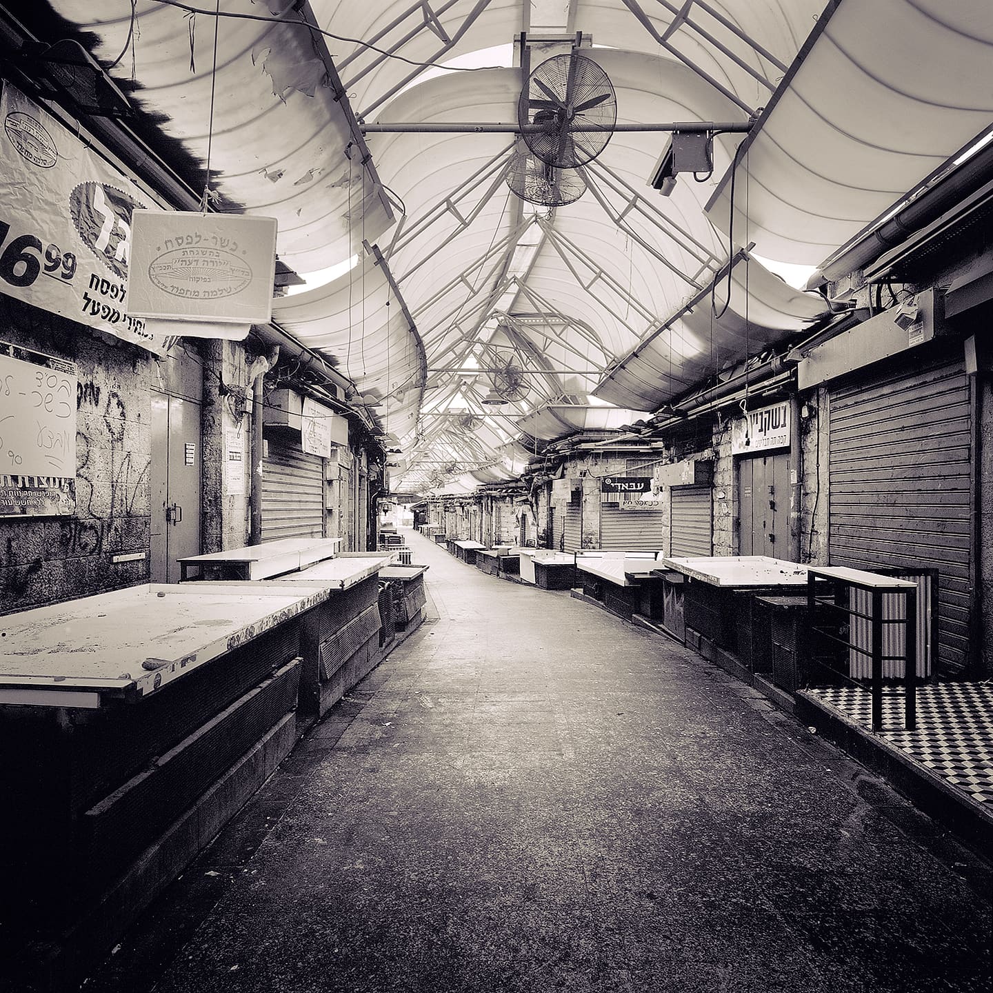 Deserted covered market aisle of empty stone counters and shuttered stalls under a fabric canopy roof