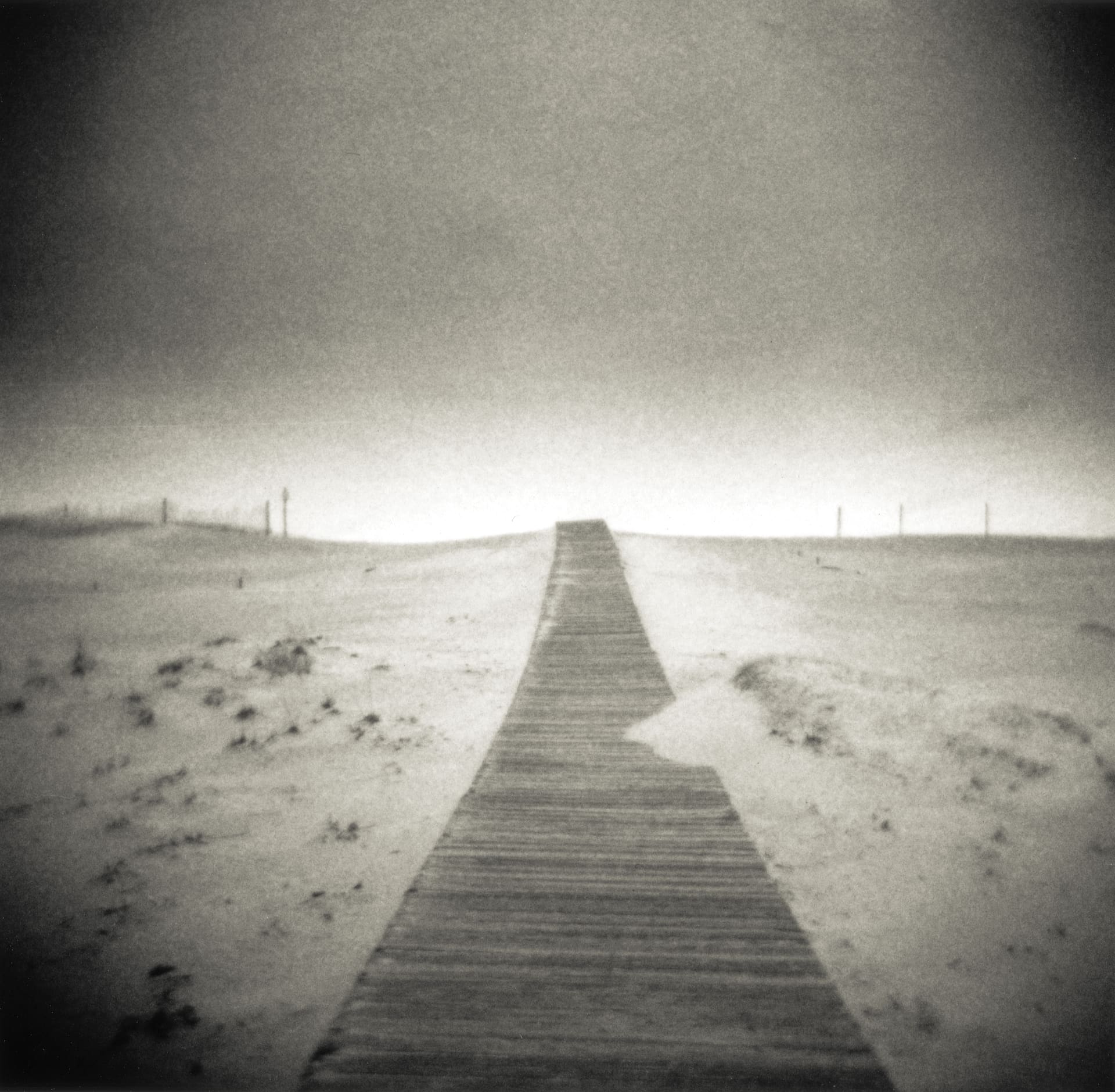 Timber boardwalk running straight over low dunes toward a bright empty horizon, marram tufts on either side