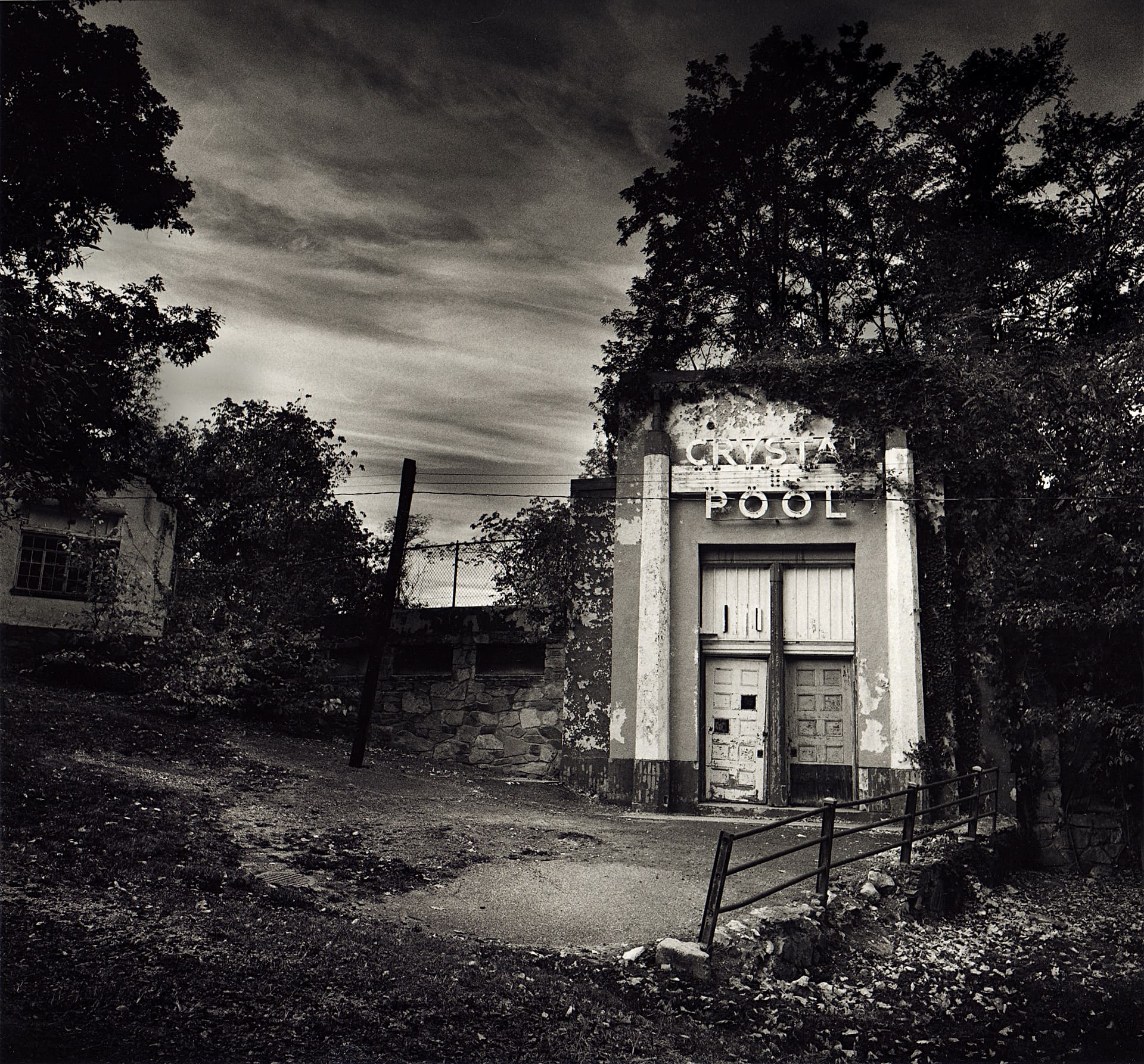 Derelict Crystal Pool entrance with peeling paint, boarded doors and ivy climbing the facade under streaked cloud