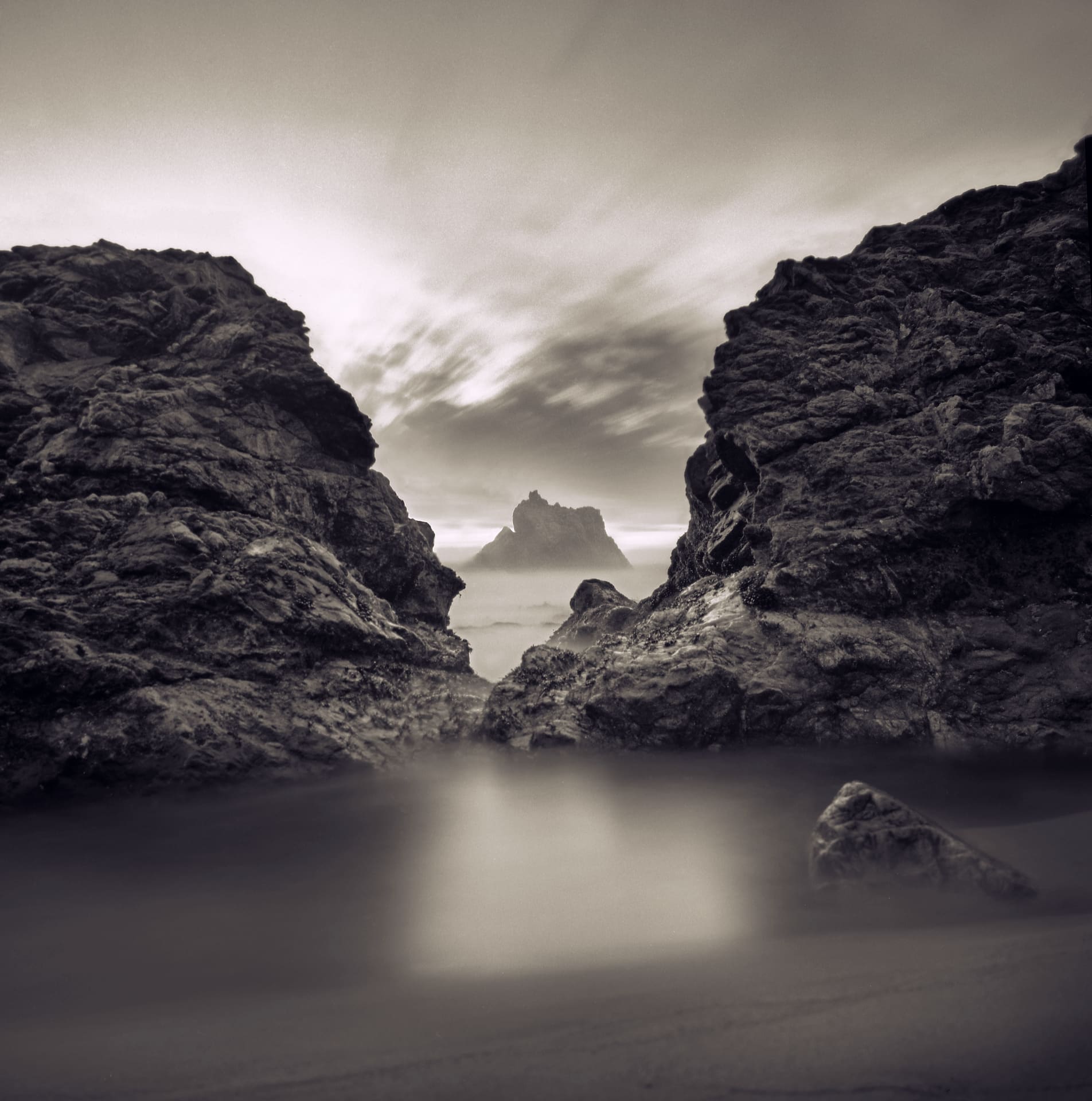Rocky cove opening to a distant sea stack, long exposure blurring surf into mist and streaking cloud