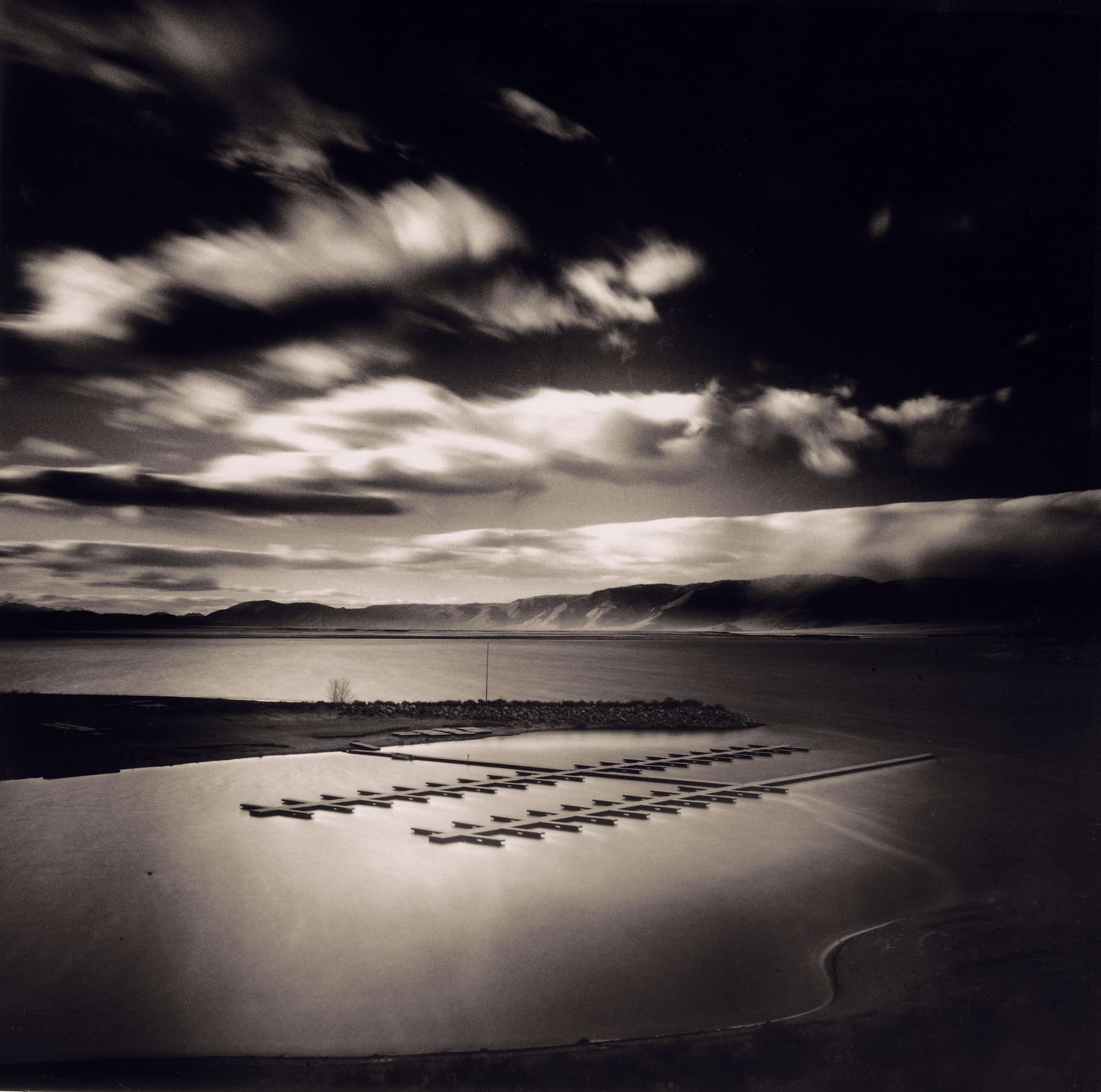 Empty floating docks on a calm lake at dusk, banded cloud above distant ridgeline, long exposure